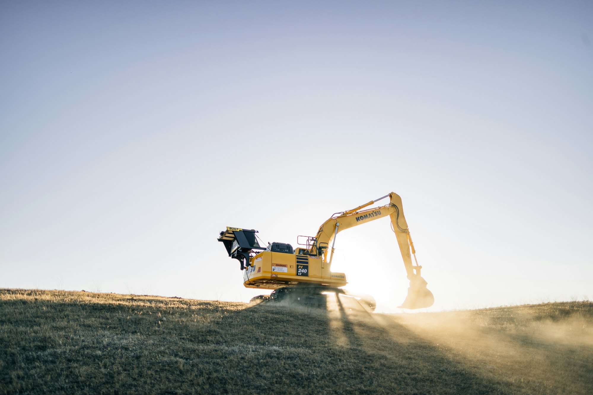 Excavator silhouetted against sunrise dust
